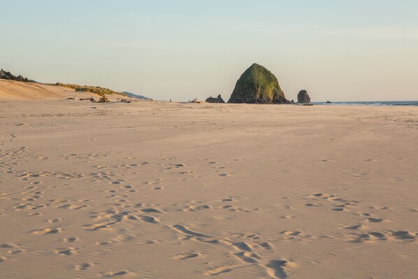 Una playa arenosa con huellas y una gran formación rocosa al fondo.