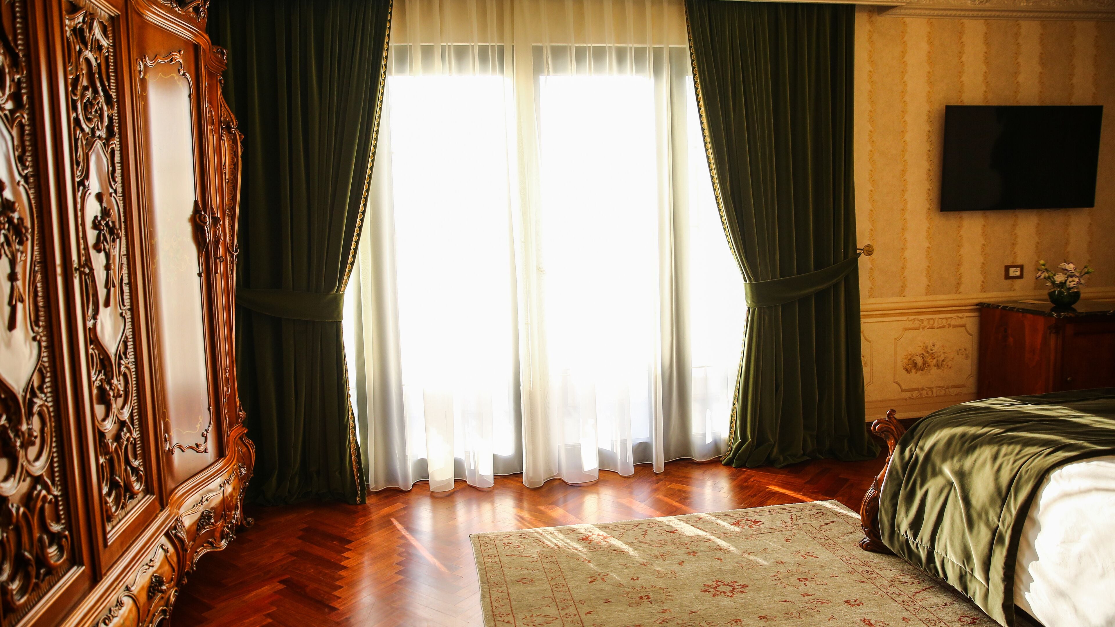 Quarto com uma grande janela, guarda-roupa de madeira, cama com colcha verde e televisão de tela plana na parede.