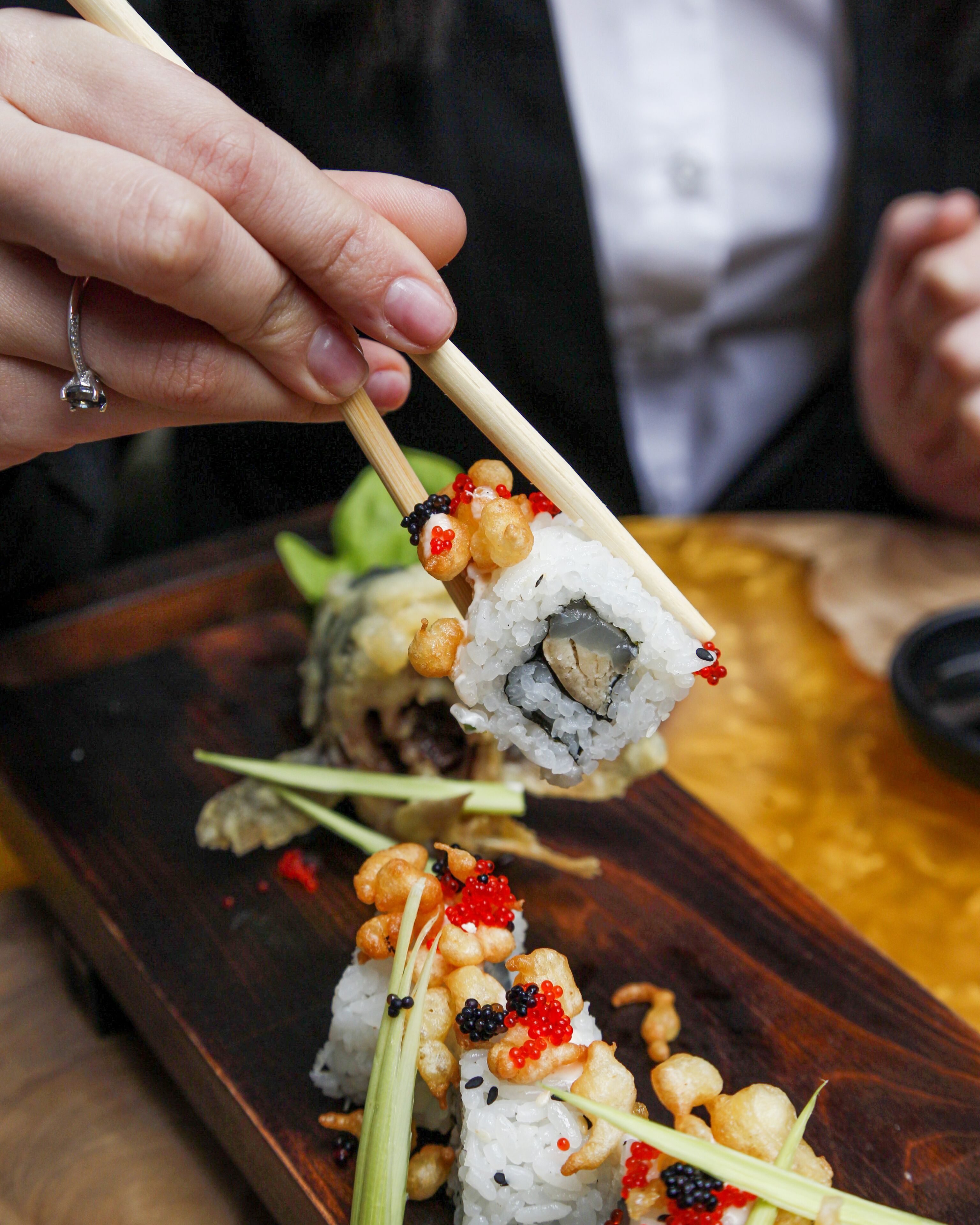 Un plato de sushi con distintos ingredientes, entre ellos huevas de pescado y una guarnición decorativa, sostenido con palillos.