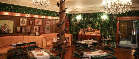 Un restaurante con paneles de madera, asientos tapizados en verde, candelabros y cuadros en las paredes.