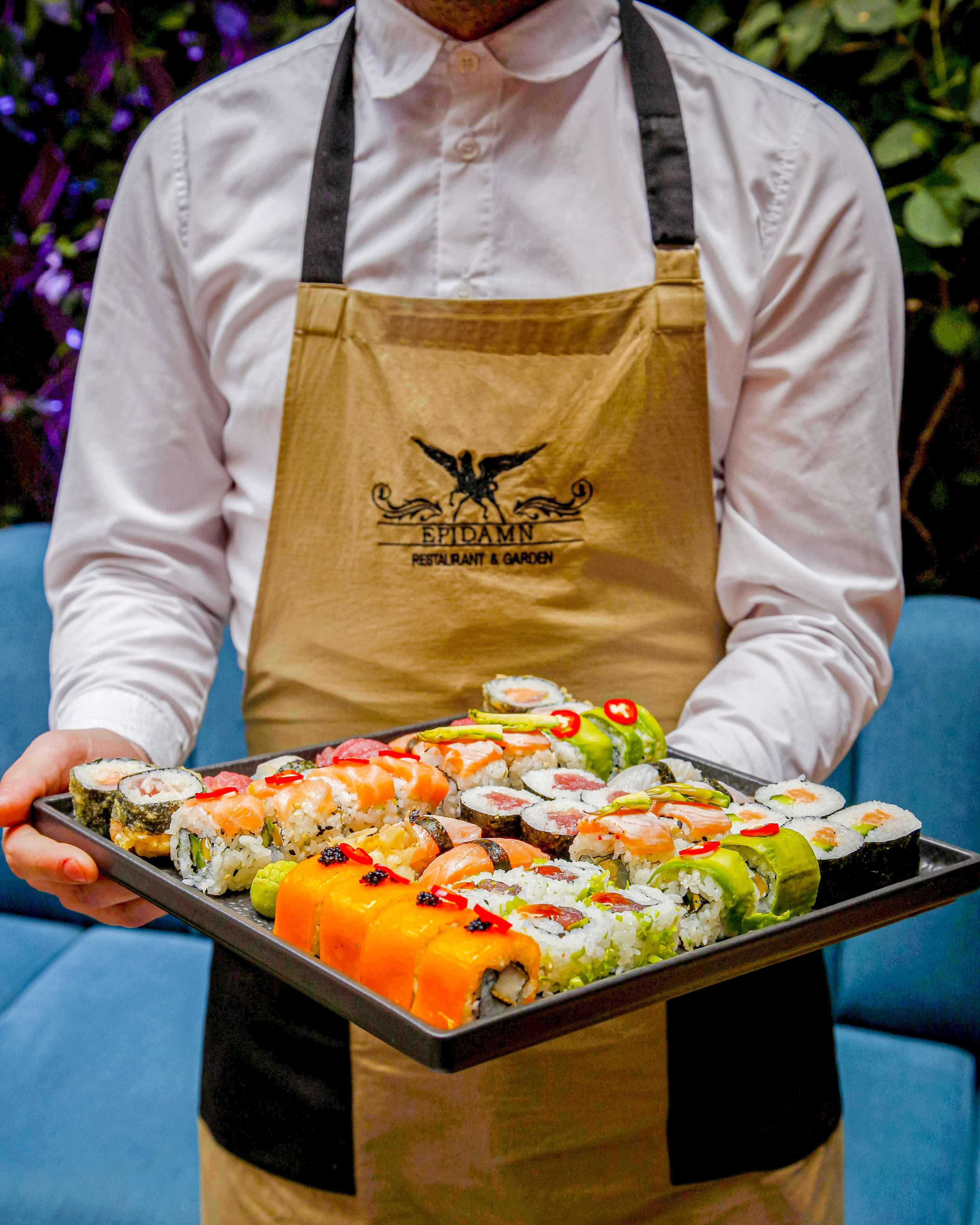 A person holding a tray of various sushi rolls.