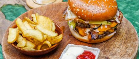 A burger with a knife in it, a glass of beer, a bowl of fries, and a small dish of ketchup and mayonnaise.