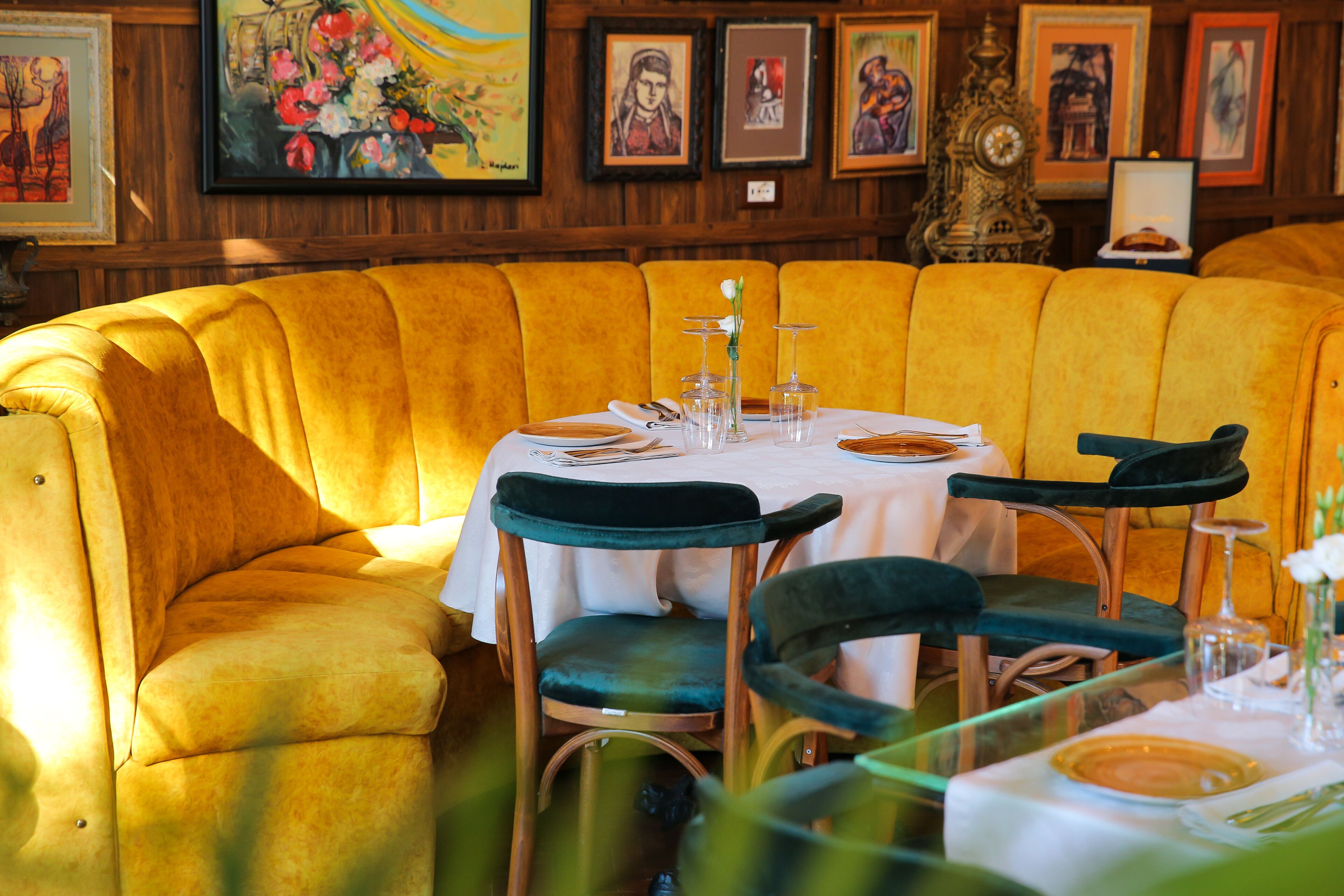 Un rincón comedor con una banca tapizada de amarillo, una mesa redonda con mantel blanco y sillas tapizadas de verde.