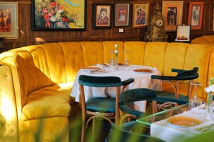 Un rincón comedor con una banca tapizada de amarillo, una mesa redonda con mantel blanco y sillas tapizadas de verde.