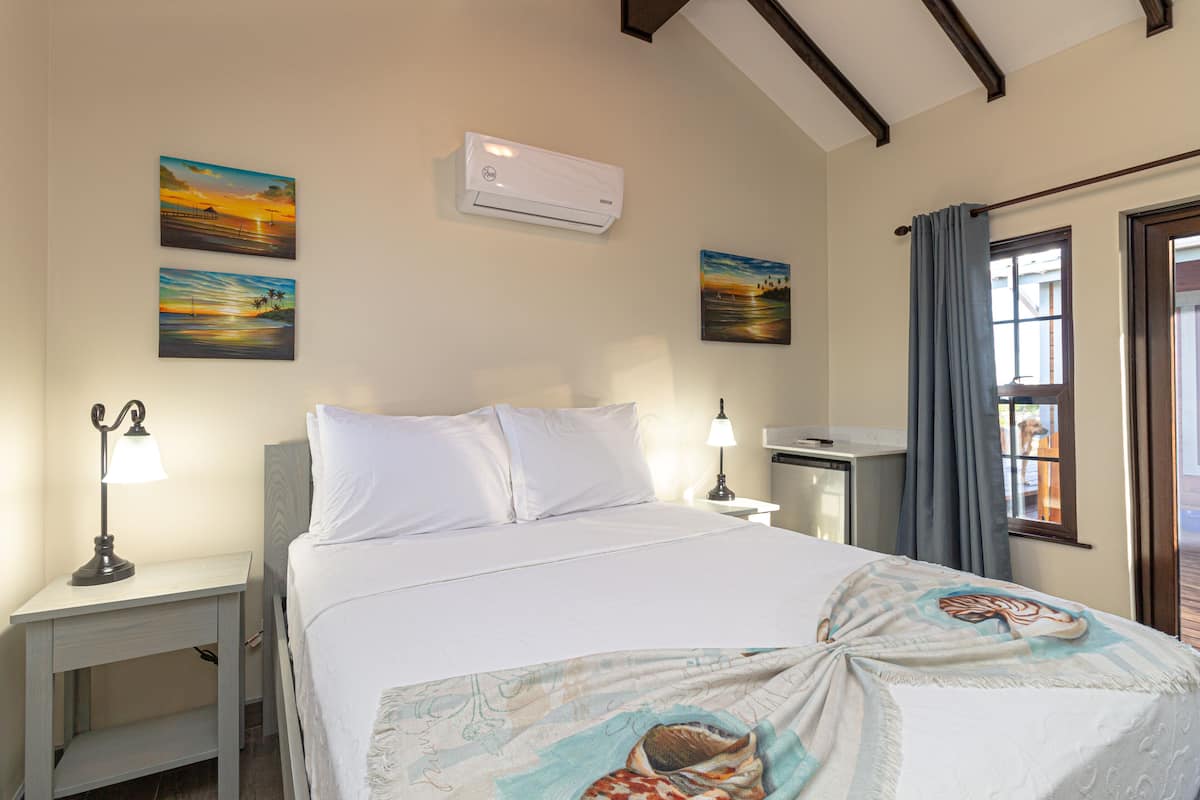 A bedroom with a bed, two bedside tables, an air conditioner, and two wall-mounted paintings.