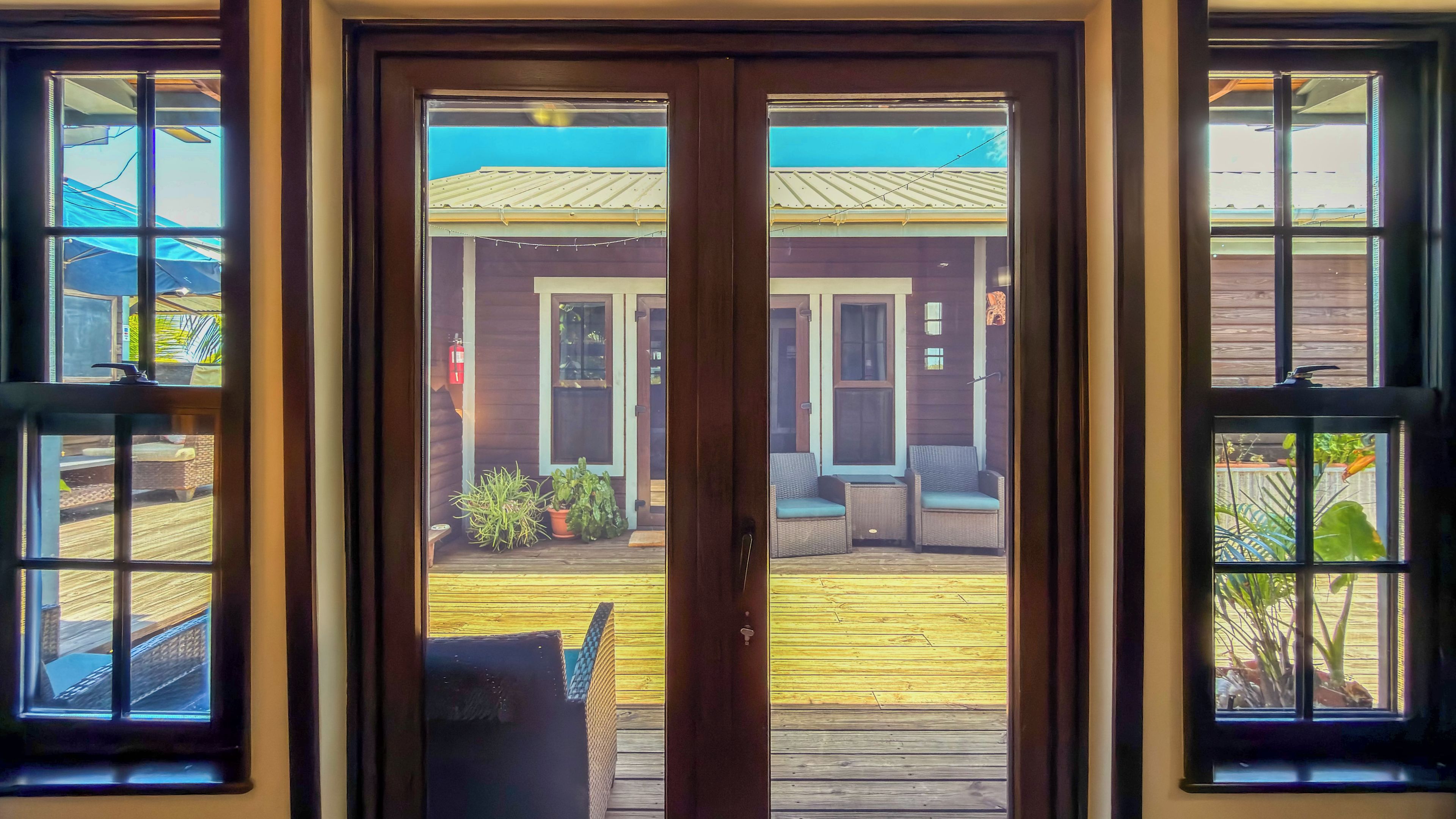 A wooden deck with outdoor seating, a fire extinguisher, and a view of a building with a metal roof.