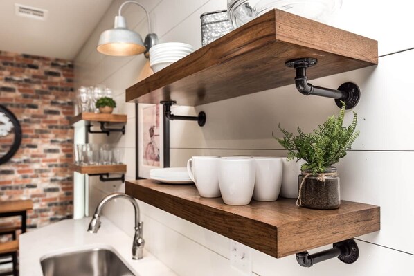 Une cuisine avec des murs en briques apparentes, des étagères en bois et un luminaire suspendu.
