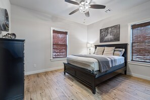 Un dormitorio con una cama, un ventilador de techo y dos ventanas con persianas.