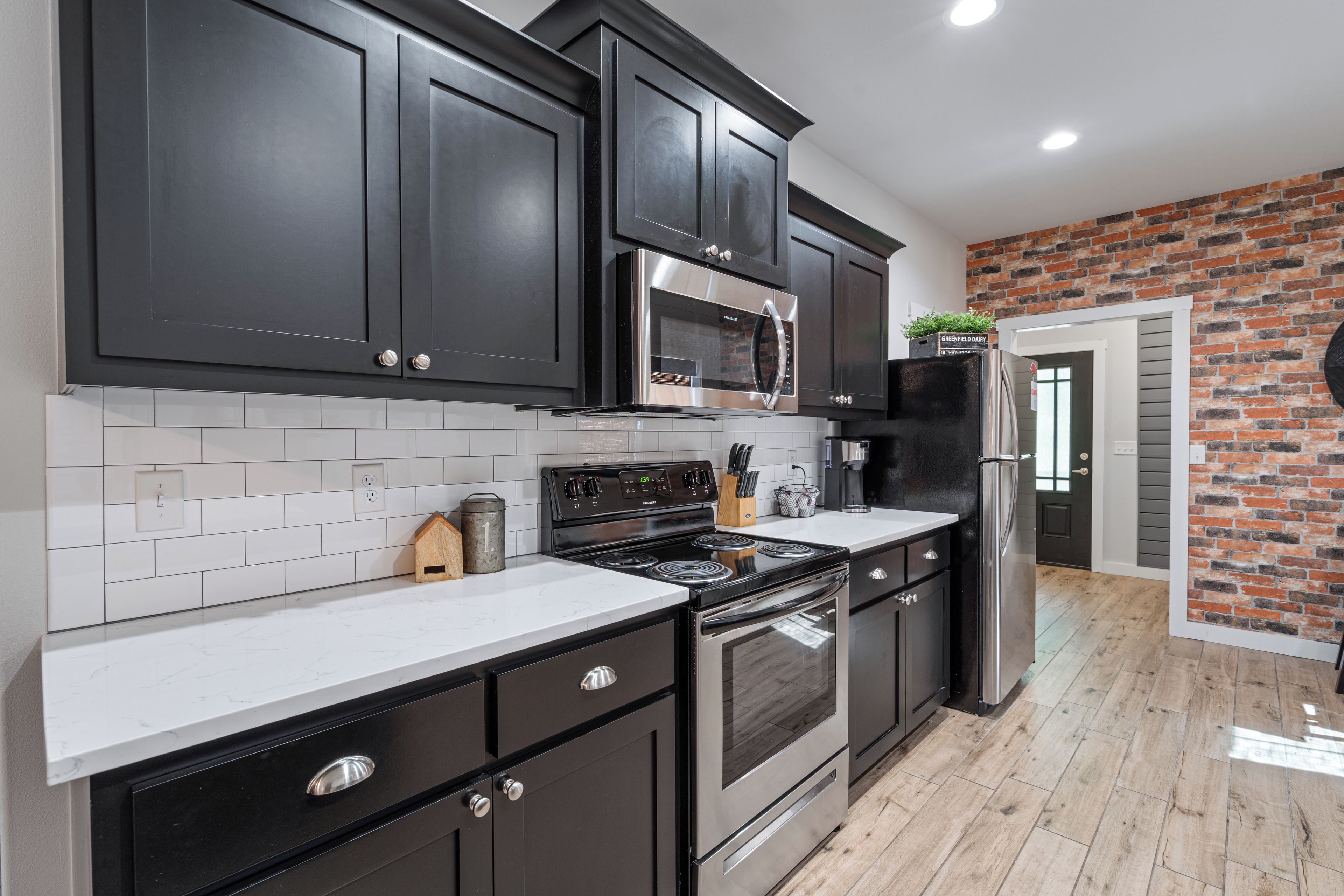 Una cocina moderna con armarios oscuros, una estufa de acero inoxidable y una pared de ladrillo decorativa.