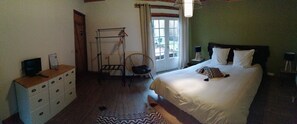 A bedroom with a bed, a chair, a dresser, a TV, and a window with curtains. - Douvilla (Douville)