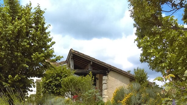 Un bâtiment rustique en pierre, doté d’un toit en pente, entouré d’un jardin luxuriant où poussent de la lavande et d’autres fleurs sauvages.