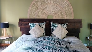 Un lit doté d’une grande tête de lit décorative, d’un mur vert et d’un ventilateur de plafond.