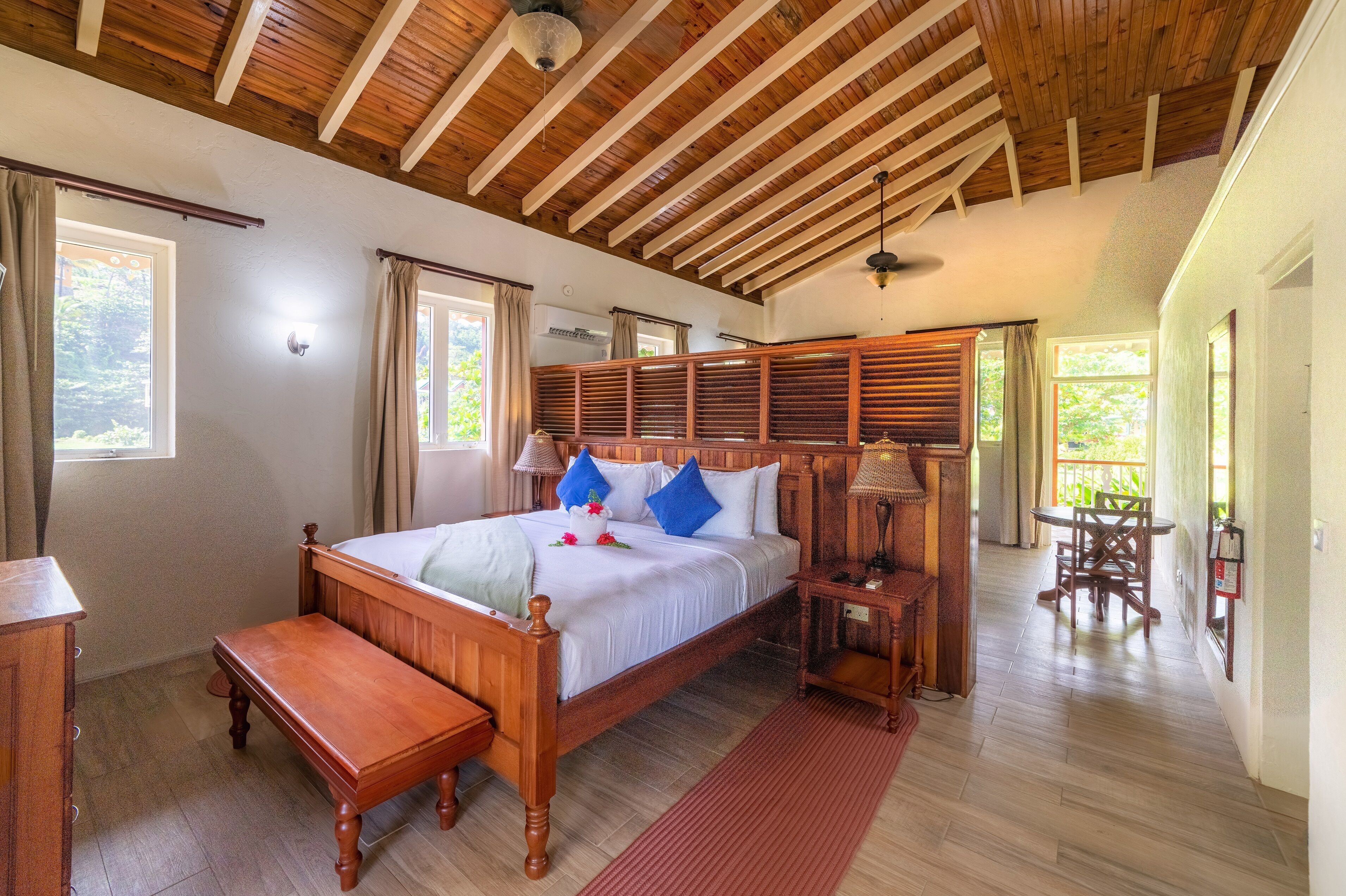 Ein geräumiges Schlafzimmer mit einem hölzernen Bett, einem Nachttisch, einer Bank und Blick ins Freie durch große Fenster.