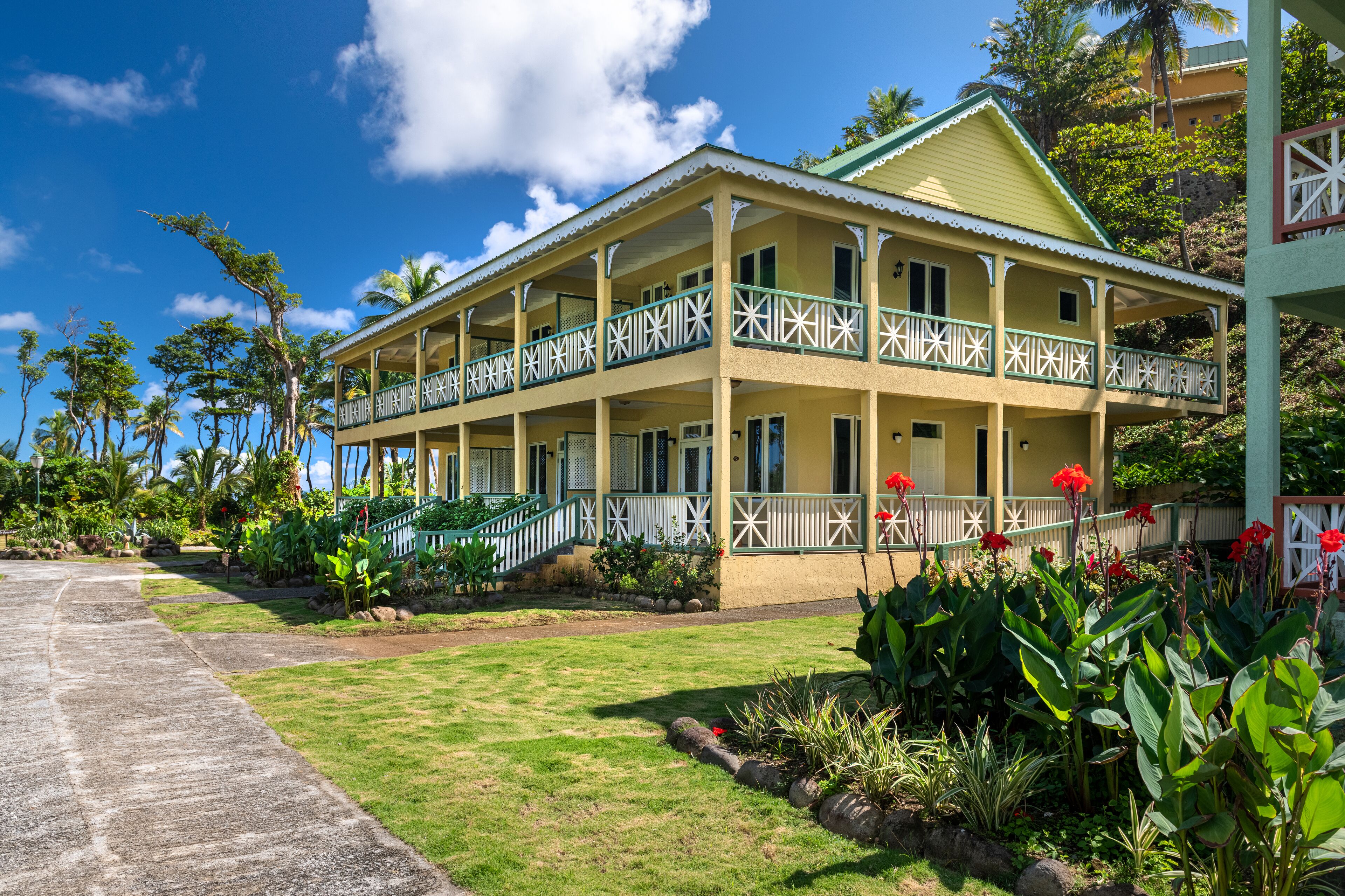 Um edifício de dois andares com varanda, rodeado por vegetação tropical e céu claro.