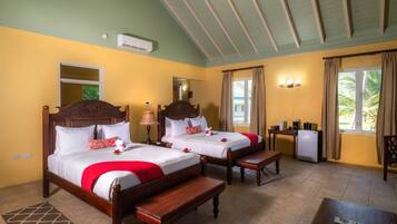 A hotel room with two wooden beds, a small desk, a refrigerator, and a window with curtains.
