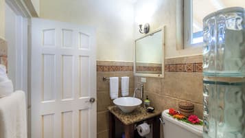 A bathroom with a white door, a sink with a mirror above it, a toilet, and a large glass jar.
