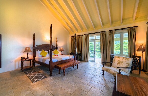 A spacious bedroom with a four-poster bed, a wooden bench, a chair, and a table. - Rosalie Bay Eco Resort & Spa (Rosalie)