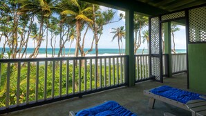 A balcony with two beds, a view of the beach, and palm trees.
