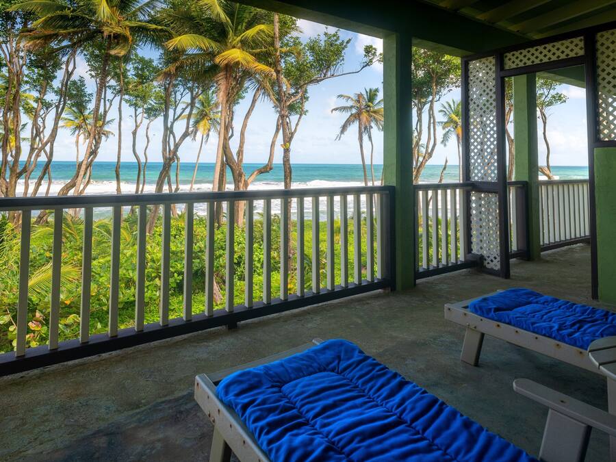 A balcony with two beds, a view of the beach, and palm trees.