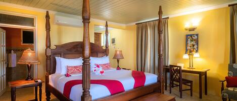 A four-poster bed with a wooden headboard, a bench at the foot of the bed, a bedside table with a lamp, and a chair with a cushion.