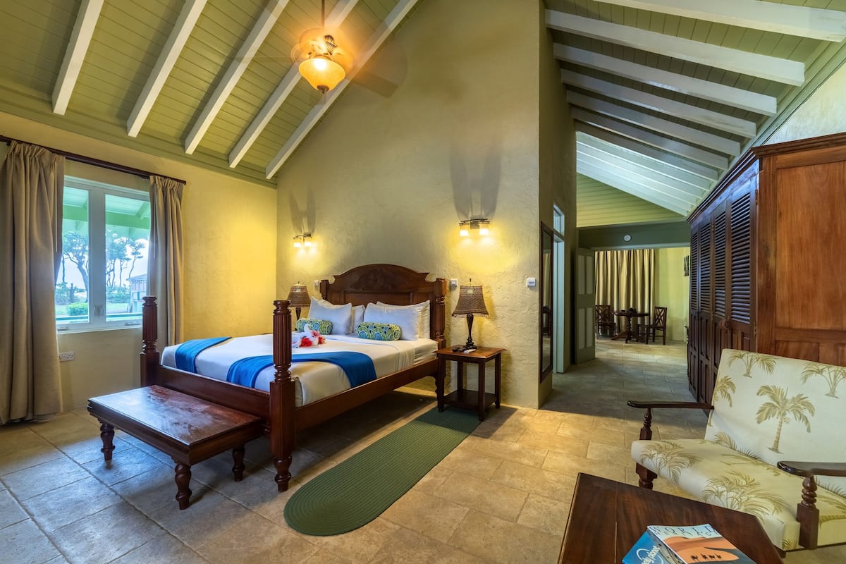 Ruime slaapkamer met een groot bed, een houten bankje, een sofa en een eethoek op de achtergrond.