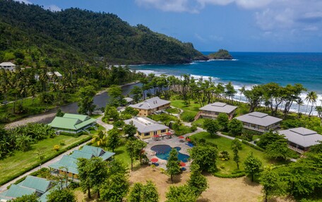 An aerial view of a resort with multiple buildings, a swimming pool, and a view of the ocean.