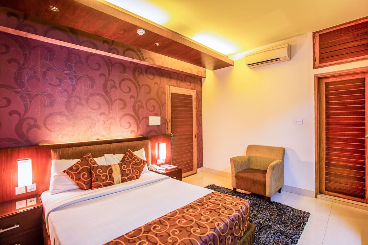A hotel room with a large bed, a chair, a nightstand, and a wall-mounted air conditioner.