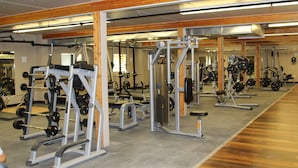 A gym with various exercise equipment, wooden beams on the ceiling, and a large mirror reflecting the space. - Target Hospitality-Midland Lodge (Midland)
