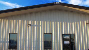 A building with vertical siding, a black door with a sign reading "11412 W. County Rd 33 Midland TX 79707 FRONT OFFICE", and two windows.