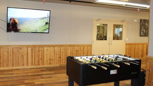 A room with a foosball table, a television mounted on the wall, and a wooden panel wall. - Target Hospitality-Midland Lodge (Midland)