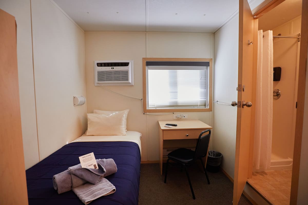 A compact hotel room with a single bed, a desk, a chair, and a shower.