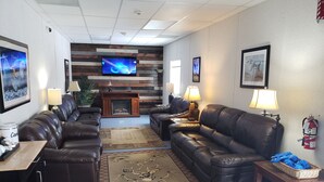 A modern living room with leather sofas, a fireplace, a flat-screen TV, and a fire extinguisher on the wall. - Target Hospitality-Williams County Lodge (Williston)