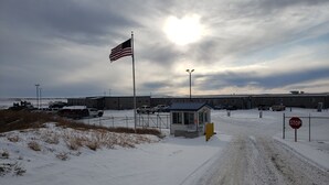 A snow-covered parking lot with a small guardhouse, a stop sign, and a flagpole with an American flag. - Target Hospitality-Williams County Lodge (Williston)