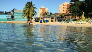 Una playa con agua cristalina, palmeras y un bar.