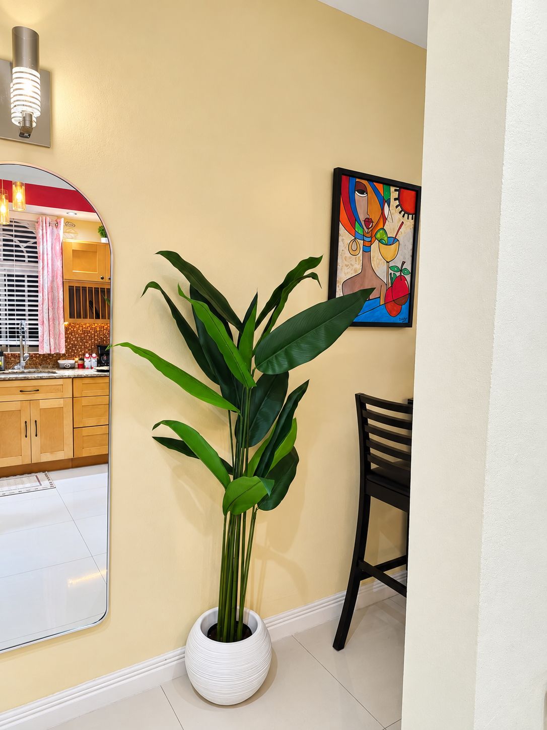 A potted plant in a white pot, a framed artwork on the wall, and a kitchen area with wooden cabinets and a countertop.
