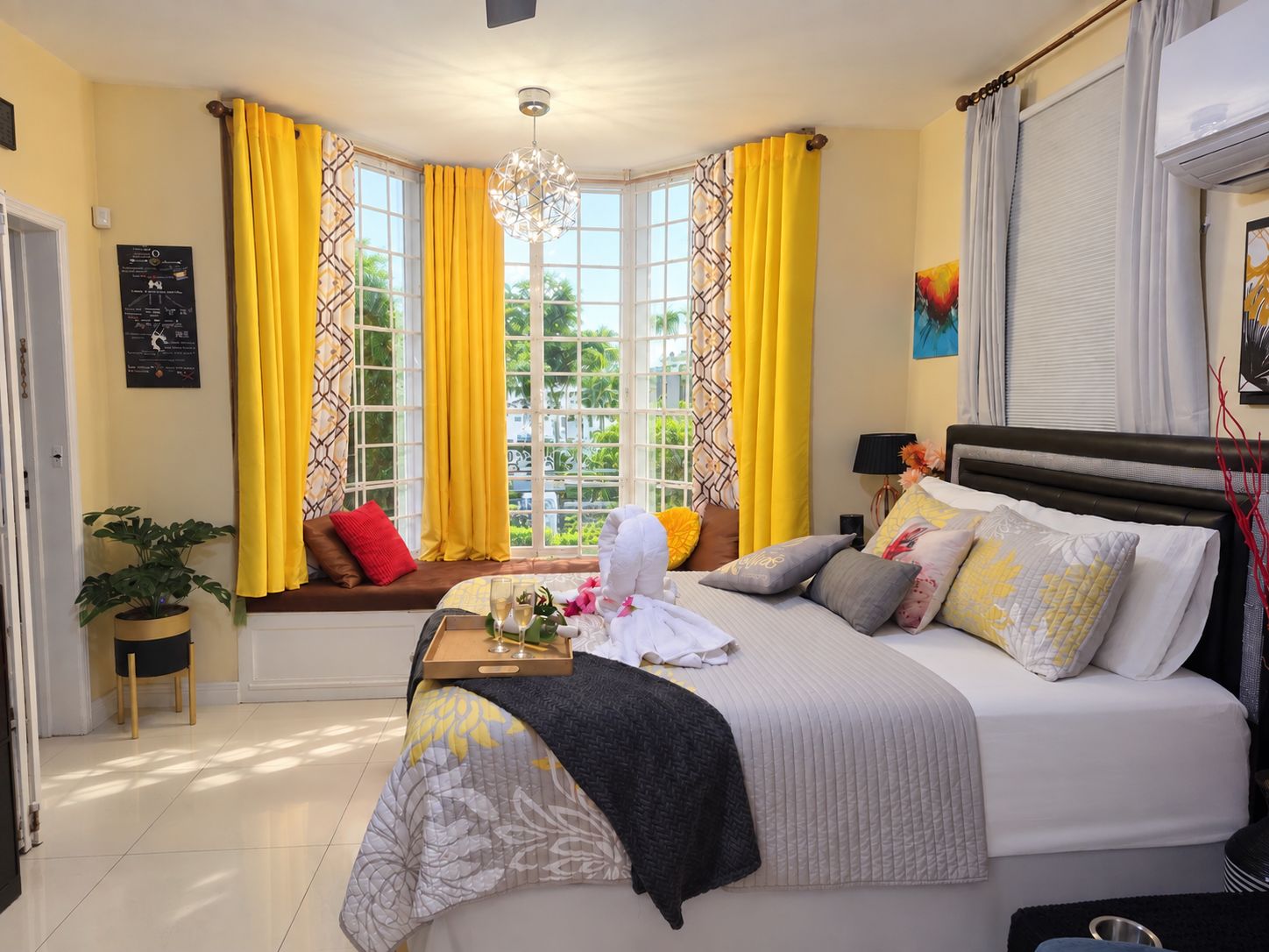 Une chambre à coucher avec un lit, un coin fenêtre aménagé en siège, une plante en pot et un lustre.