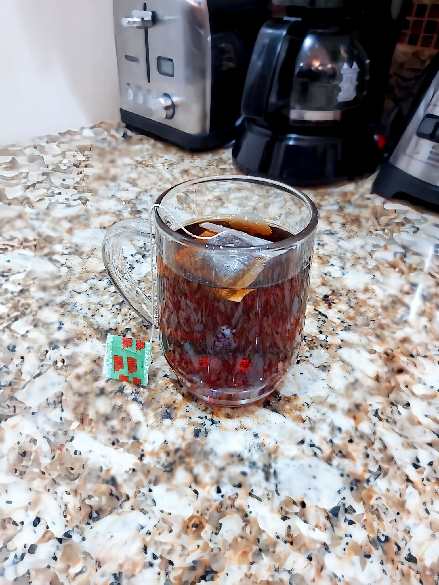 Una taza de vidrio con una bolsita de té sobre una encimera moteada.