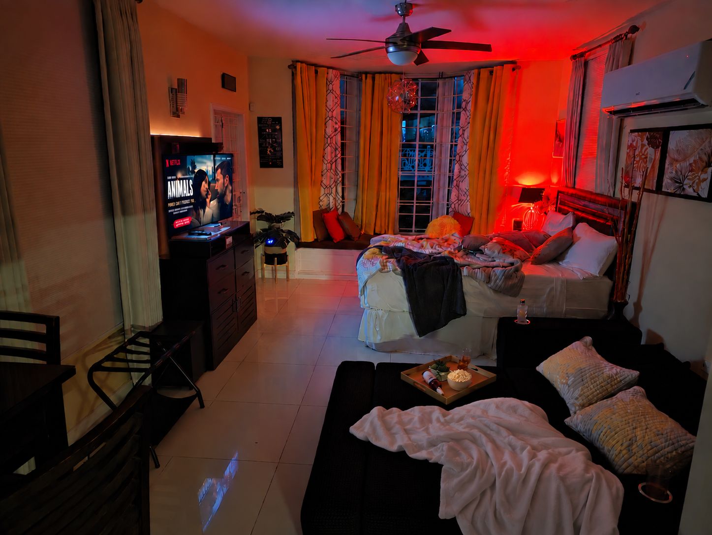 Ein Zimmer mit einem Bett, einem Schlafsofa, einem Fernseher und einem Deckenventilator.
