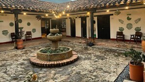 A courtyard with a stone fountain, potted plants, and a tiled roof. -  Hotel Aceitunos (Villa de Leyva)