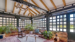 A covered patio area with wooden beams, potted plants, a rocking chair, a small table, and a cat house. -  Hotel Aceitunos (Villa de Leyva)