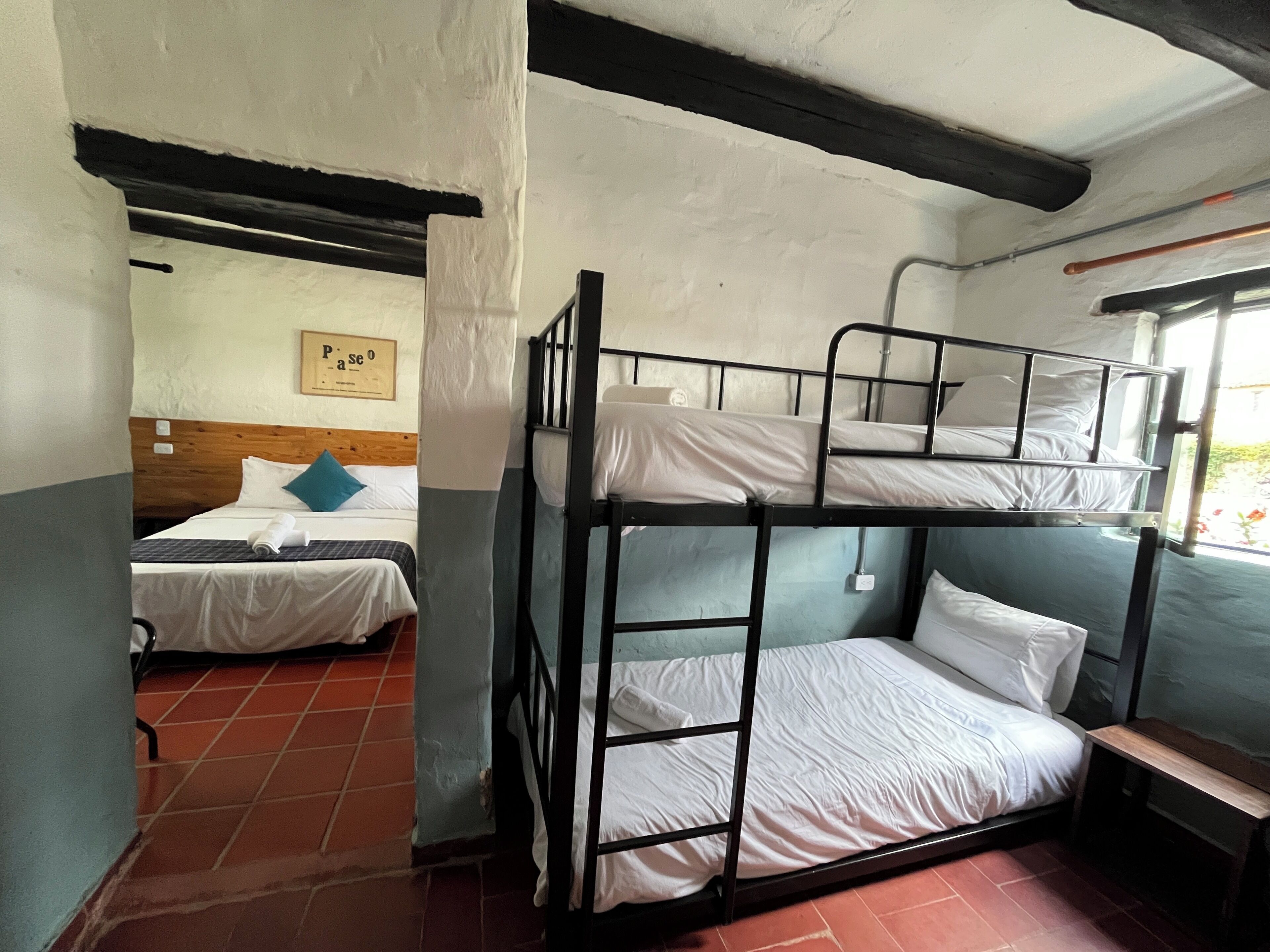 Een studentenkamer met stapelbedden, een houten hoofdeinde, een betegelde vloer en een lijst met een afbeelding erop.