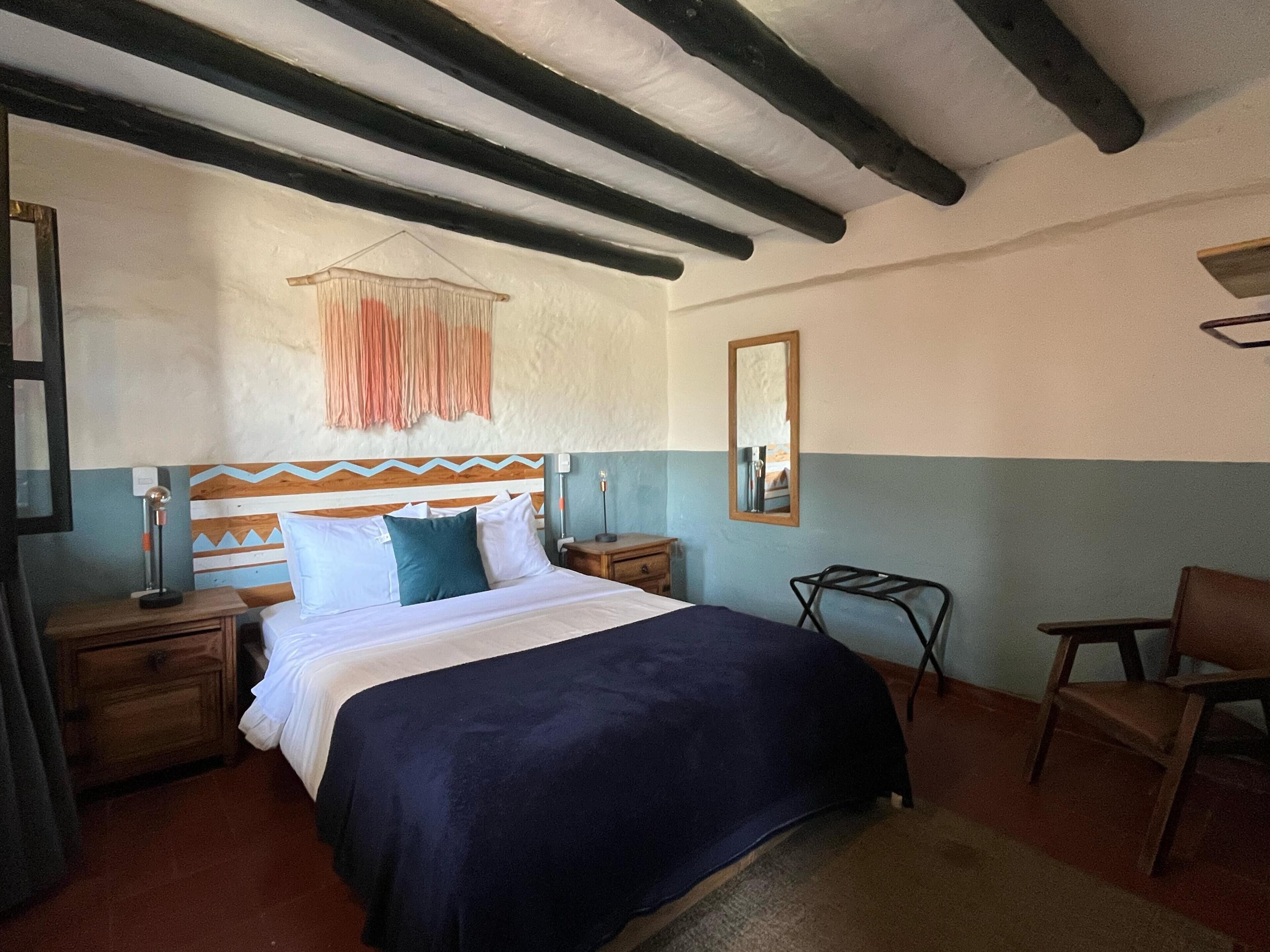 A bedroom with a bed, bedside tables, a chair, a hanging light fixture, and a mirror on the wall.