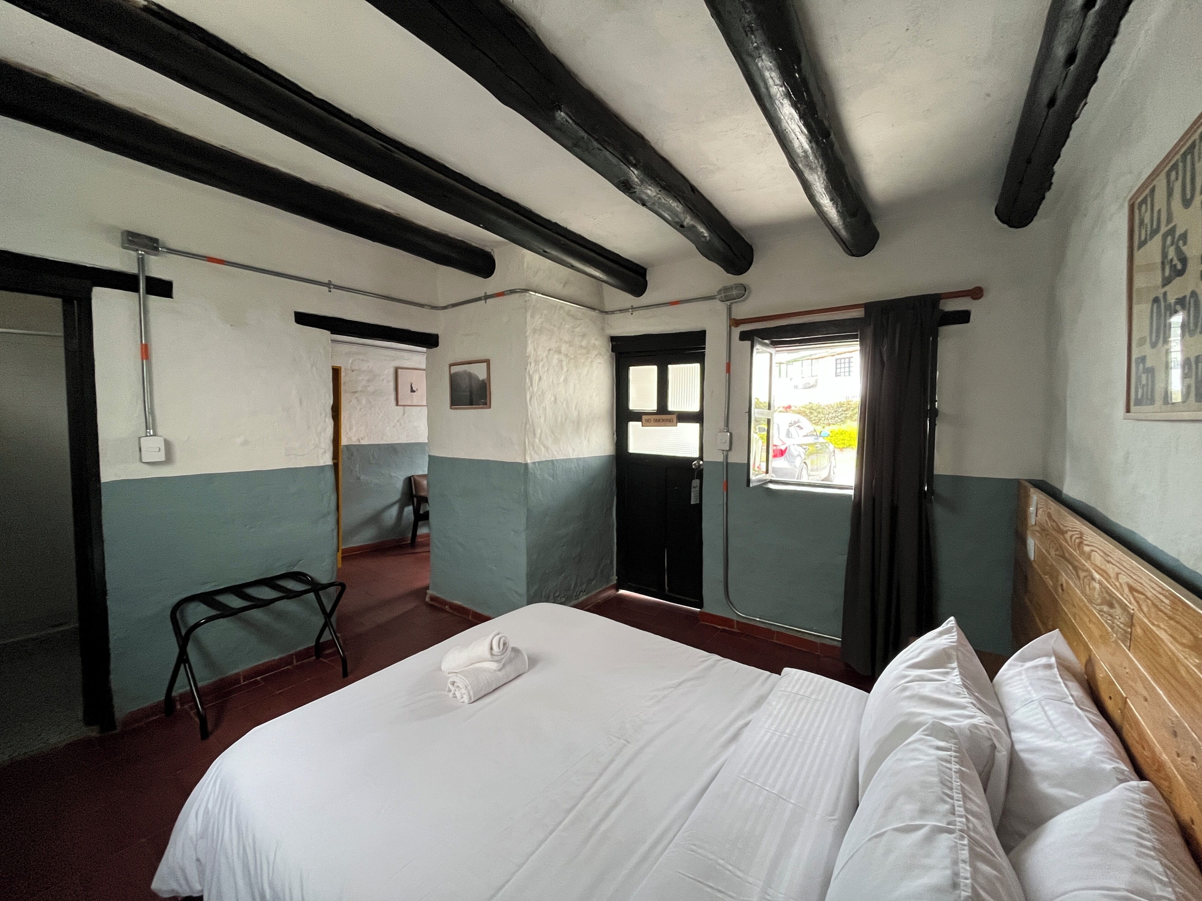 Ein Zimmer mit Bett, Tür, Fenster und Kleiderhaken.