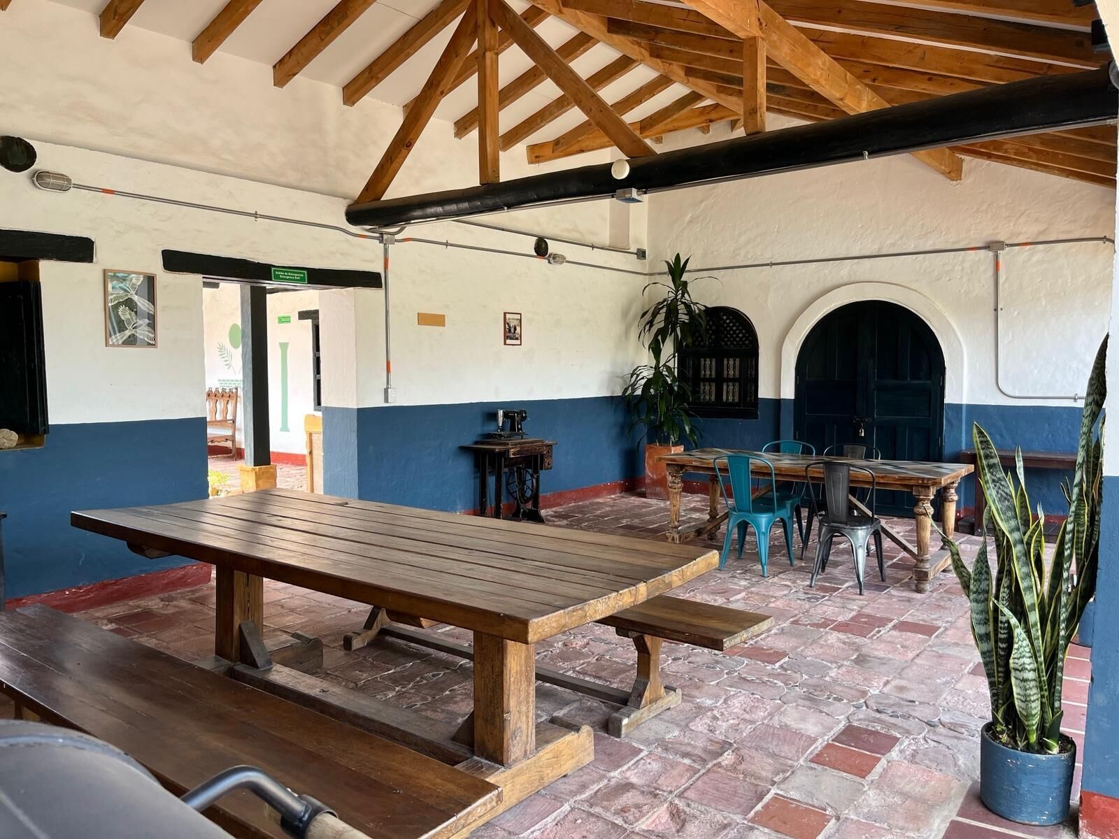 A rustic interior with wooden beams, a large wooden table, and a potted plant.
