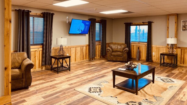 A furnished living room with a television, wooden furniture, and a patterned rug. - Target Hospitality-Odessa West Lodge (Notrees)