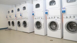 A row of stacked front-loading washing machines in a commercial laundry room. - Target Hospitality-Watford City Lodge (Watford City)