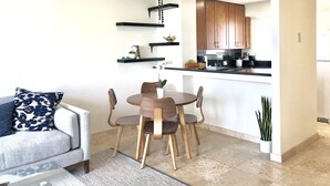 Een moderne keuken met houten kastjes, een eethoek met een ronde tafel en stoelen, een plafondventilator en een klein kookeiland met een spoelbak.