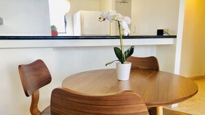Een ronde houten eettafel met vier stoelen, een potorkidee en een witte koelkast op de achtergrond.