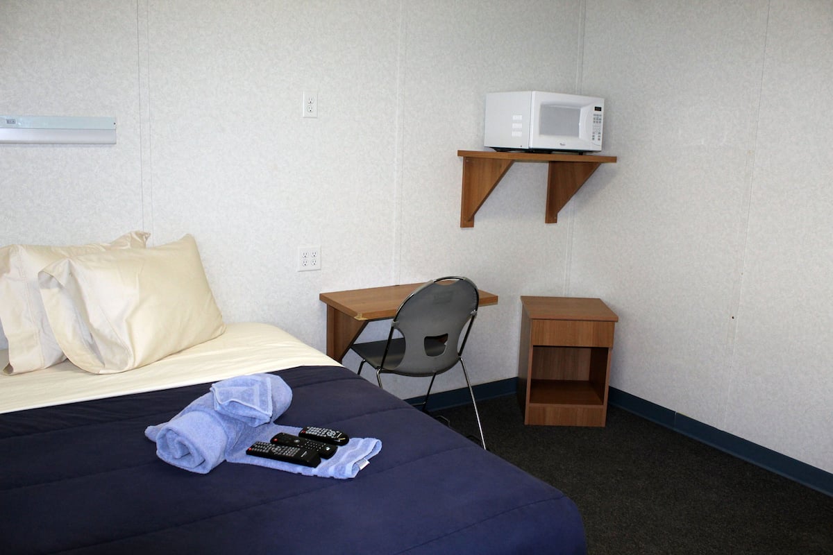 Een hotelkamer met een bed, een bureau, een stoel, een magnetron en een klein houten nachtkastje.