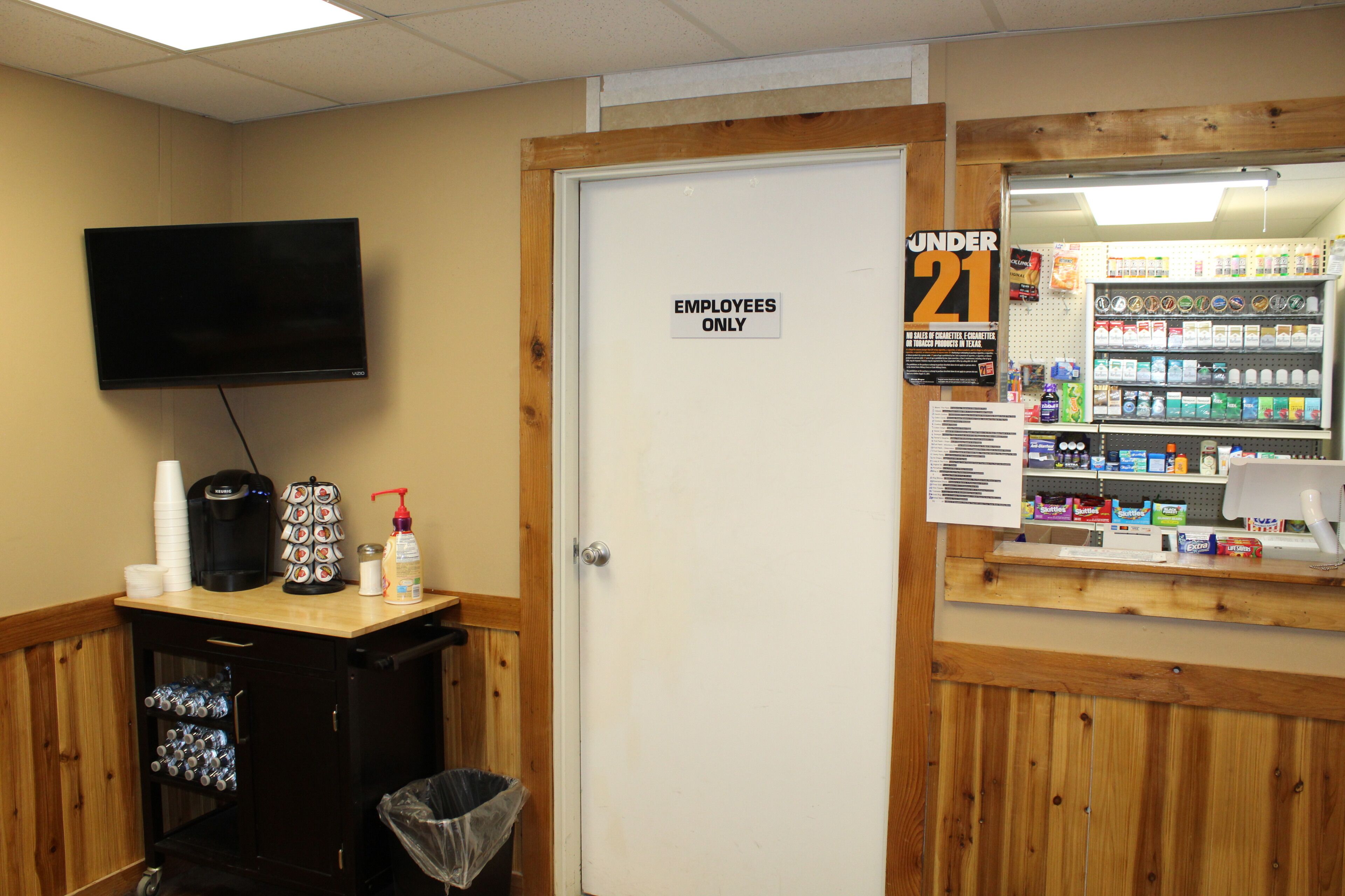 A room with a closed door labeled "EMPLOYEES ONLY," a television mounted on the wall, a vending machine, and a small counter with snacks and drinks.